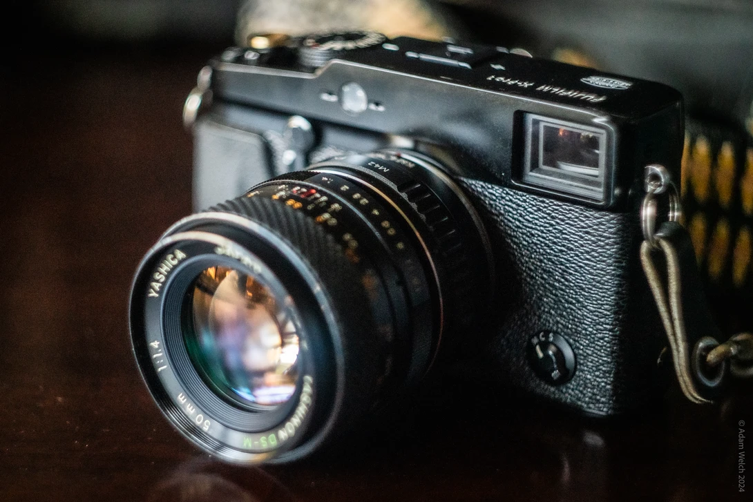 Vintage rangefinder camera with textured black body and fast prime lens, displayed against blurred background.