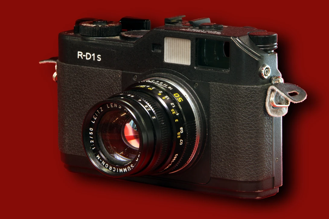 Leica R-D1s rangefinder camera with Carl Zeiss lens against red background.