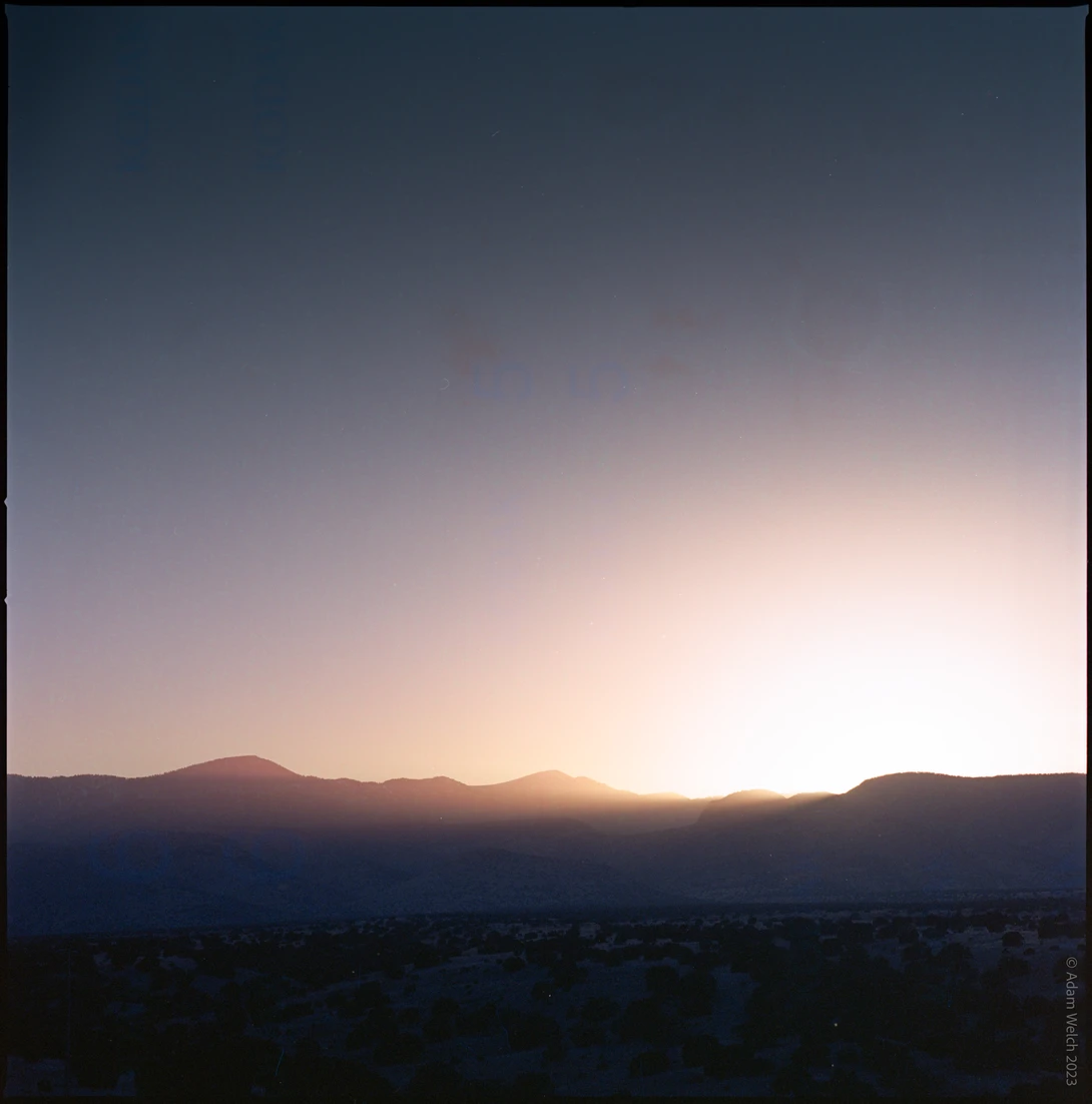Silhouetted mountain range at sunrise with warm golden light breaking through the horizon.