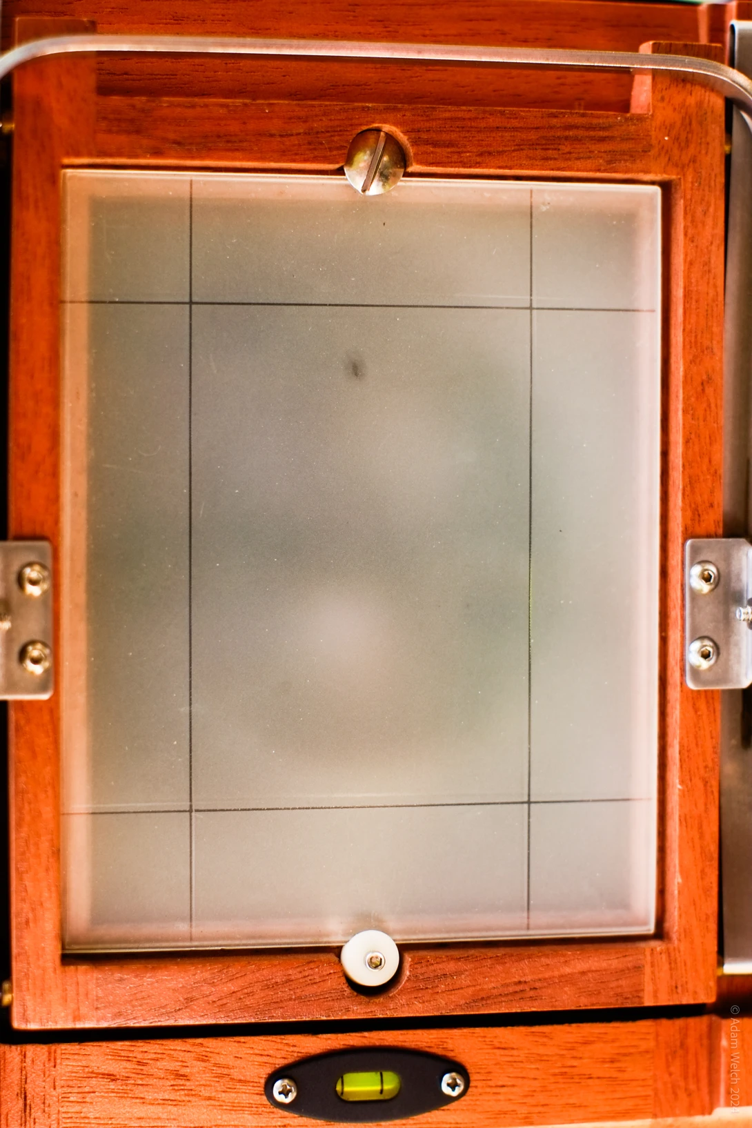 Orange wooden view camera with frosted glass focusing screen and metal knobs on dark background.