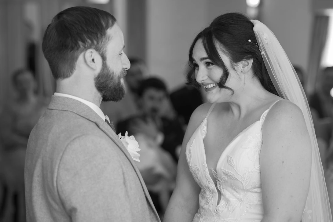 Bride and groom exchanging vows during wedding ceremony, smiling at each other in black and white.