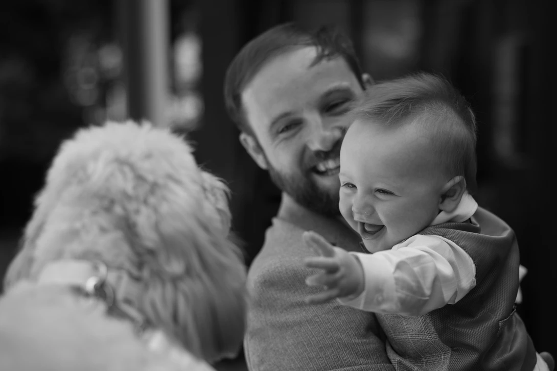Man holding a smiling toddler while petting a fluffy white dog.