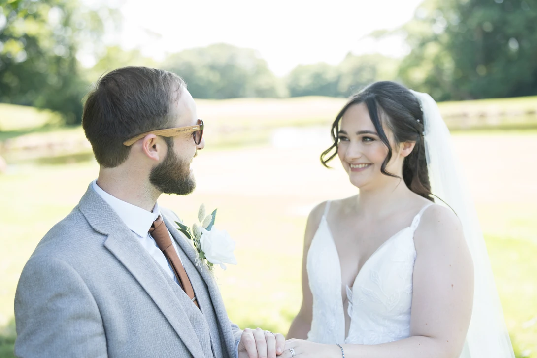 Bride and groom facing each other outdoors during ceremony with green field background.
