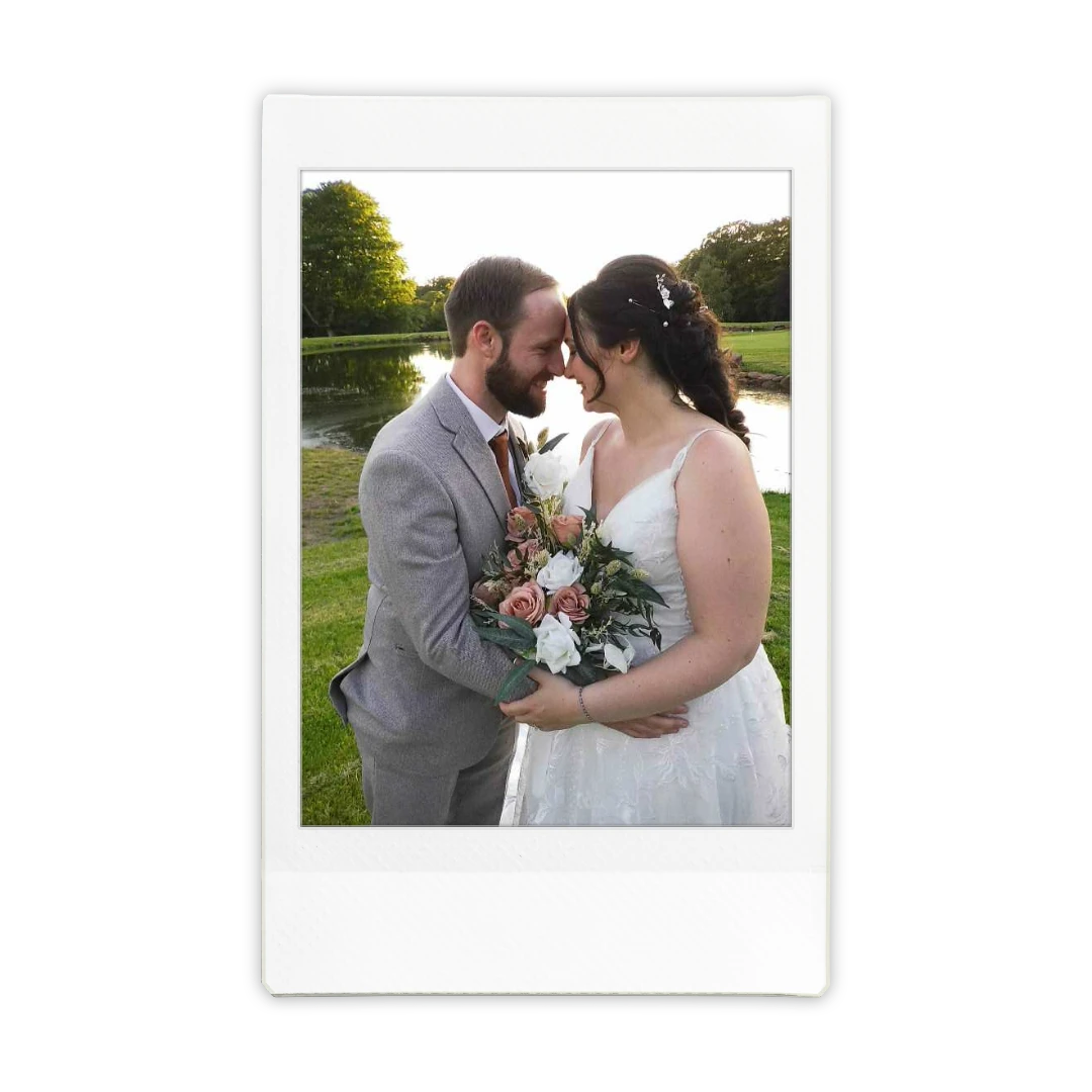 Bride and groom embracing outdoors while holding a white and pink bouquet, photographed in Polaroid instant film format.