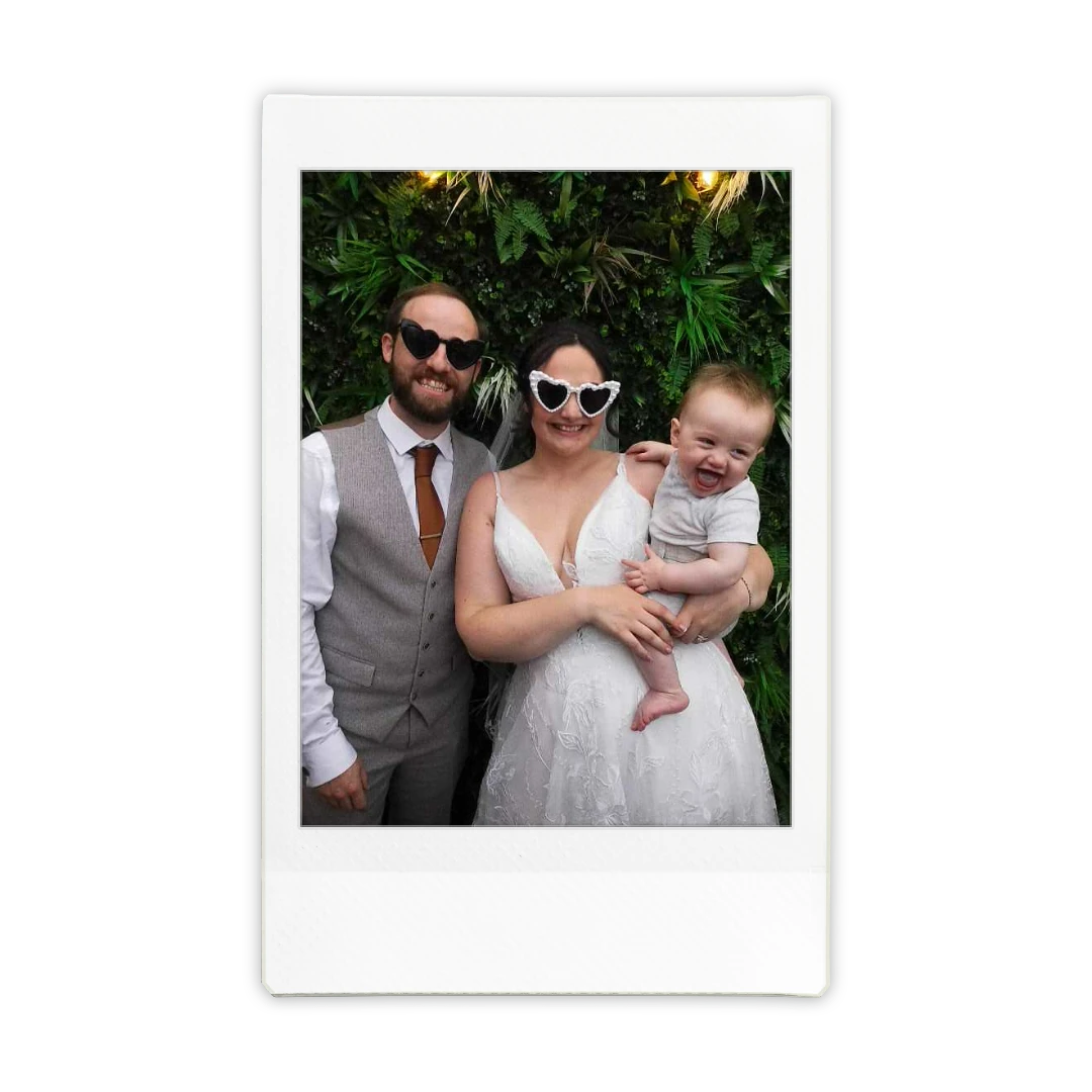 Family of three wearing sunglasses posed together outdoors with green foliage background.