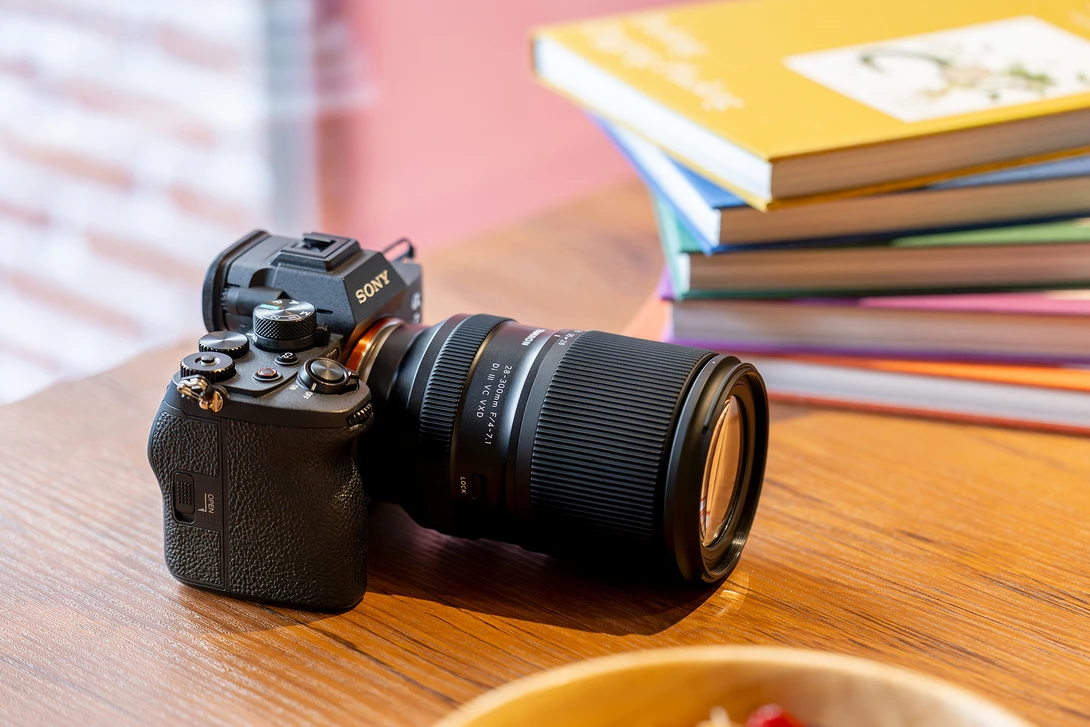 Sony mirrorless camera with telephoto lens on wooden desk beside stacked colorful books.