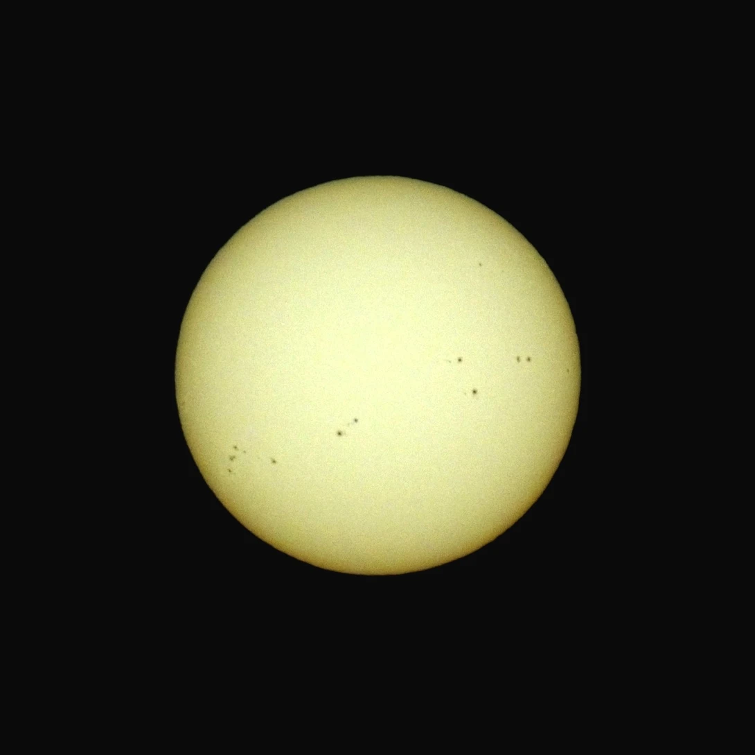Solar disk photographed against black background showing surface details and small dark sunspots.