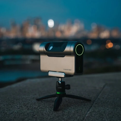 Compact mirrorless camera on tripod positioned on rooftop overlooking city skyline at dusk.