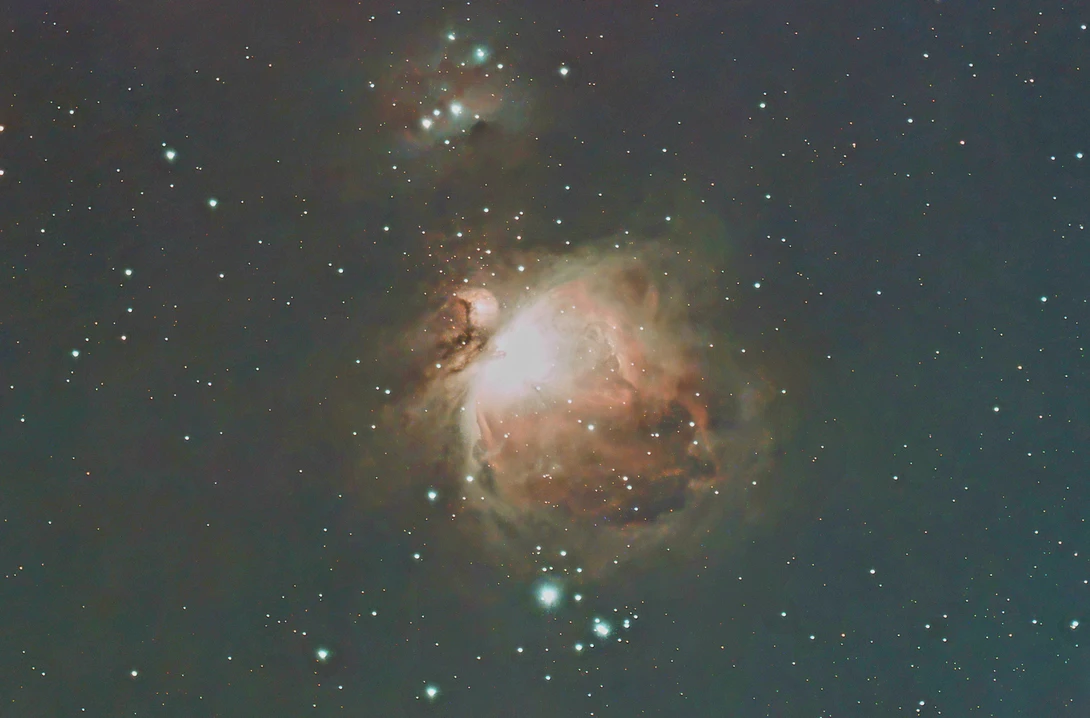 Orion Nebula captured through a telescope, showing bright central region with radiating dust clouds and surrounding stars.