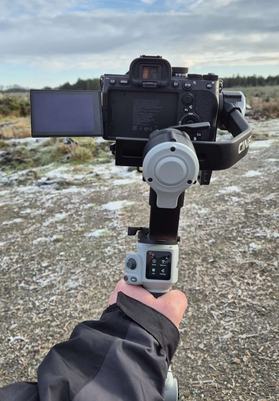 Gimbal-mounted camera rig held by operator's hand in desert landscape.