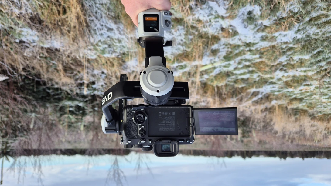 Mirrorless camera mounted on a gimbal stabilizer, held aloft over a frost-covered field.