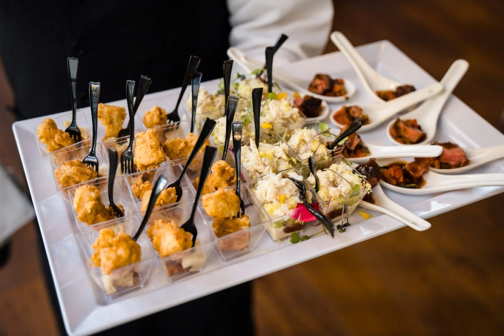 Appetizer platter with golden fried bites on small forks and creamy salad portions in white dishes.