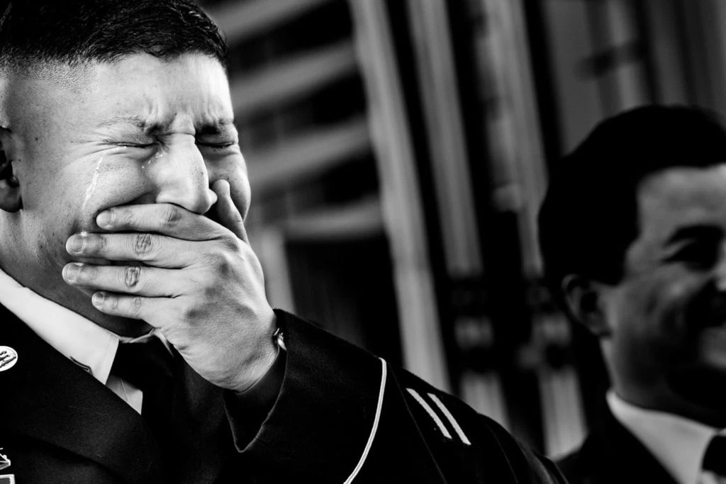 Man in formal attire with hand covering mouth, eyes closed in an expression of distress or surprise.