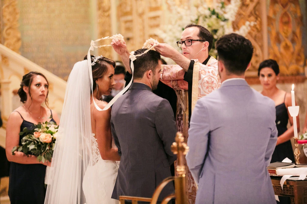 Bride and groom exchange vows at altar during wedding ceremony with officiant and wedding party present.