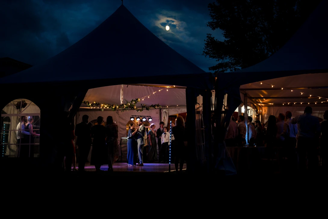 Nighttime event under illuminated tent structures with silhouetted guests and warm interior lighting against dark sky.