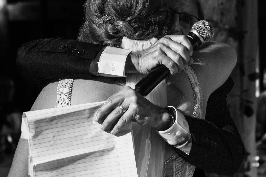 Black and white photograph of hands holding a microphone and papers during a formal event or speech.