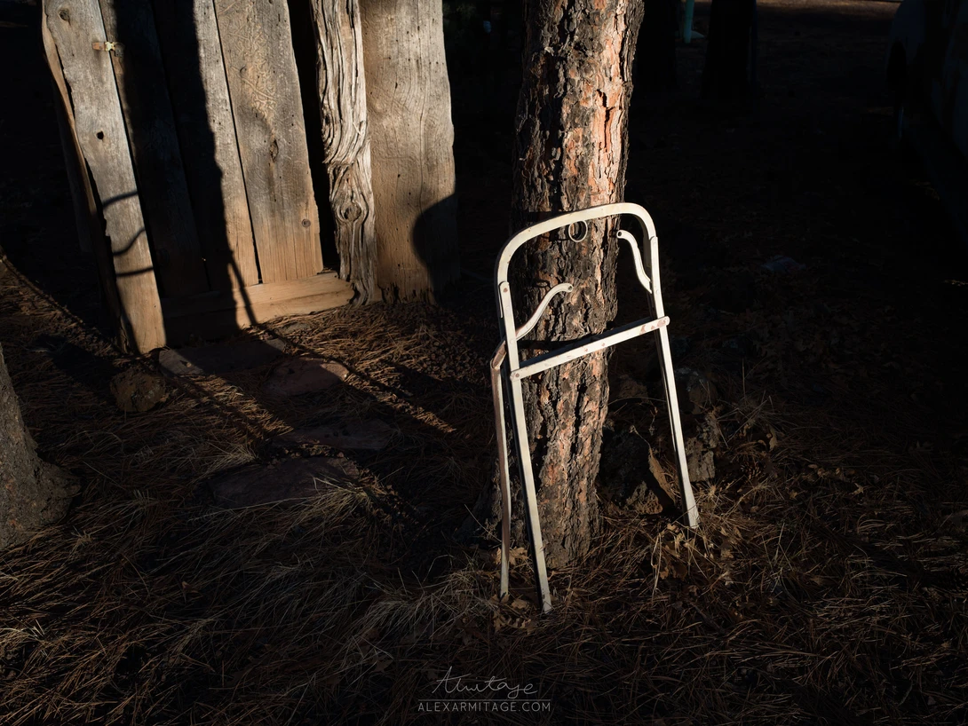 White metal hay feeder leaning against weathered wooden posts in a dark barn interior.