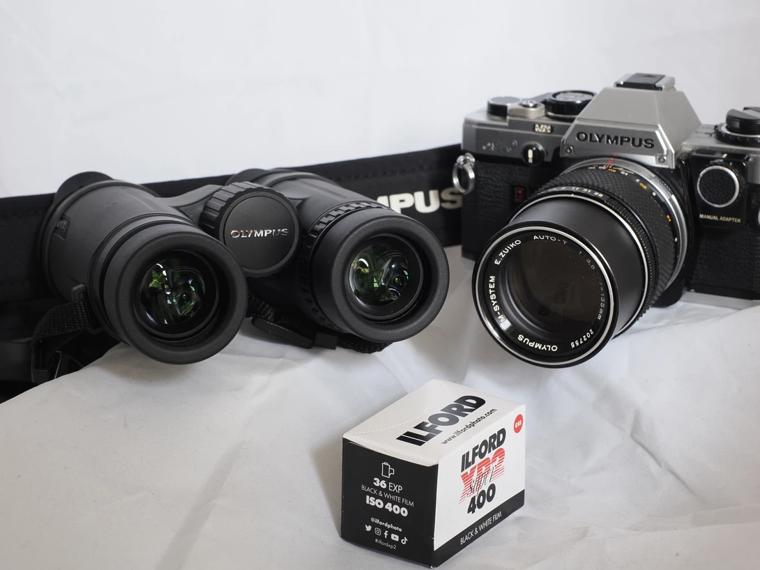 Olympus film cameras and lenses arranged on white surface with film canister.