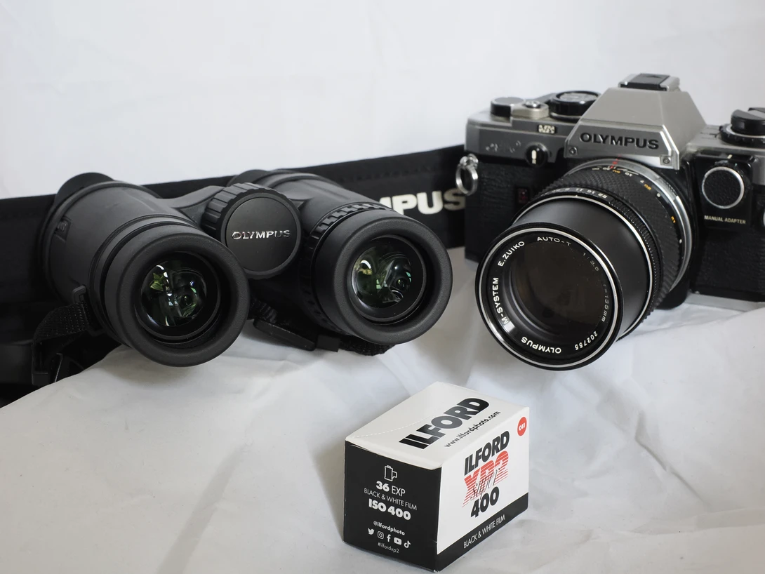 Collection of vintage Olympus film cameras and lenses with a roll of Kodak Portra 400 film.