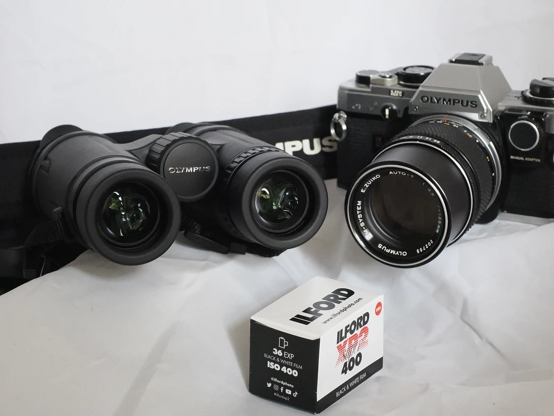 Collection of vintage Olympus film cameras and lenses with a roll of Kodak film on white background.