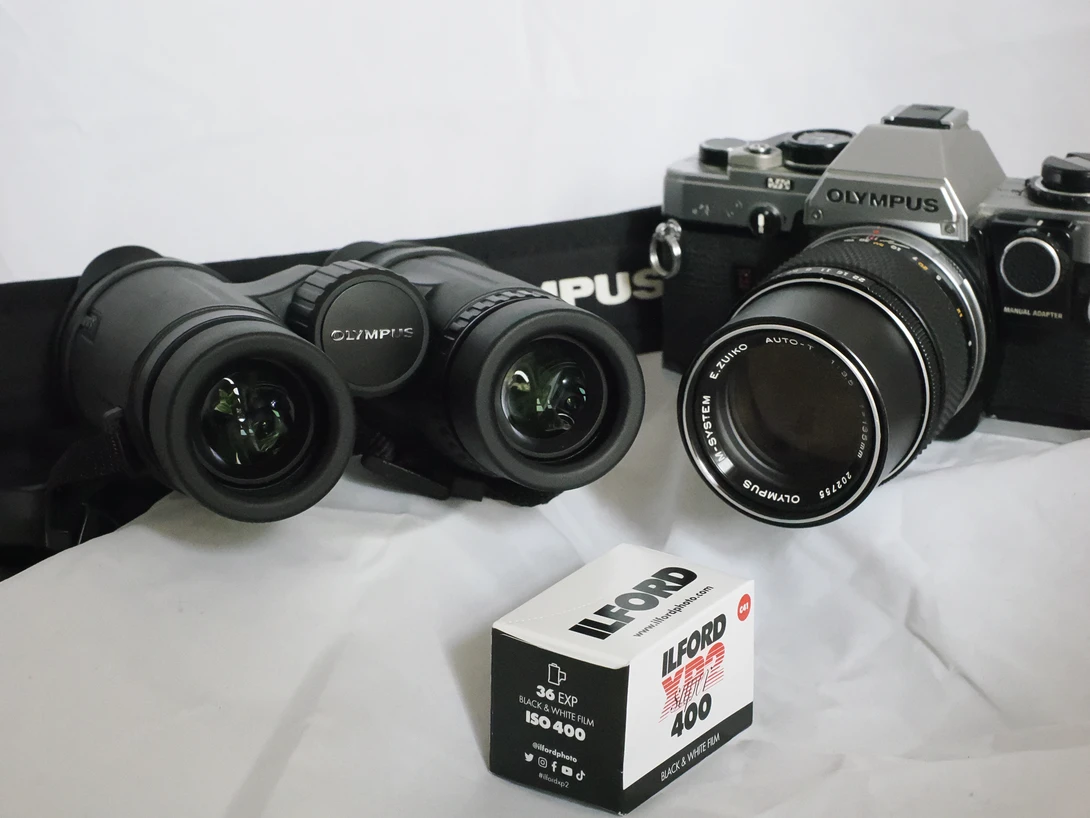 Vintage Olympus film cameras and lenses arranged with an expired film box on white background.