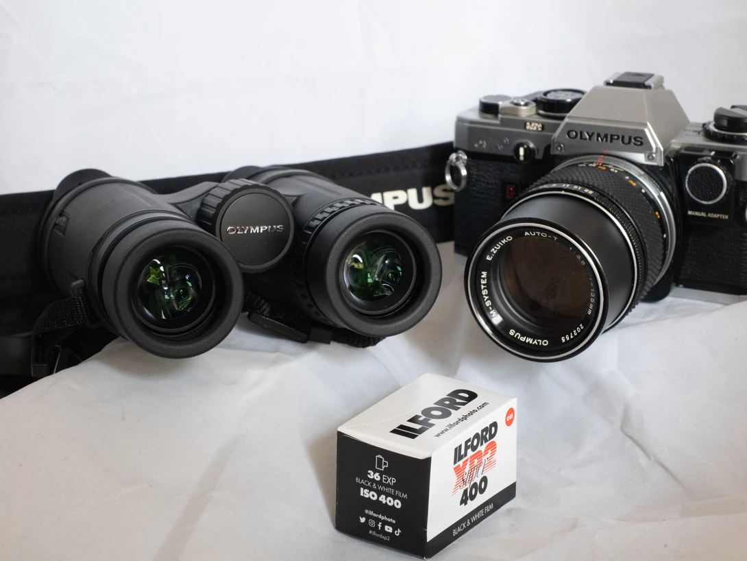 Collection of vintage Olympus film cameras and lenses arranged on white surface with film box.