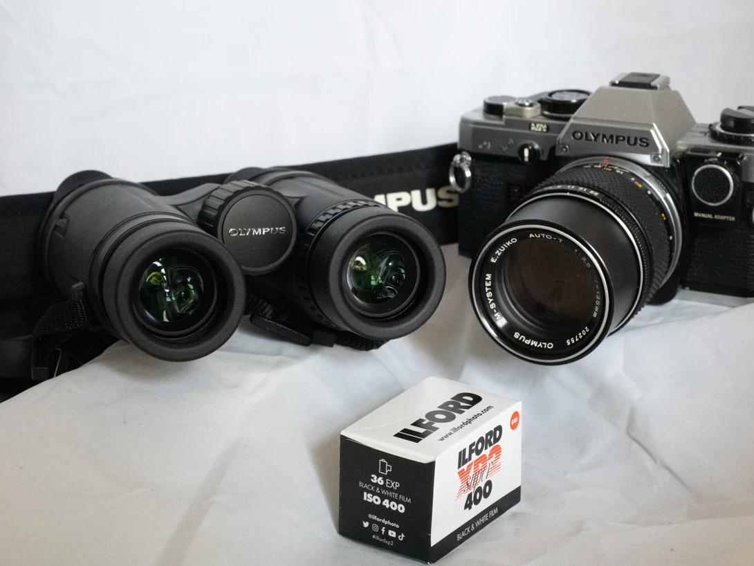 Vintage Olympus film cameras with lenses and an expired film box on white surface.