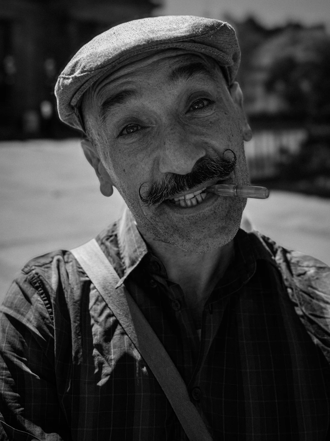 Black and white portrait of an older man with a distinctive mustache wearing a flat cap and collared shirt.