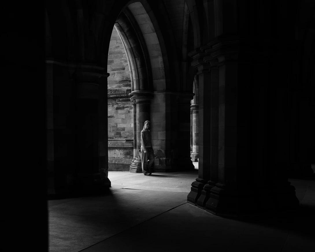 Silhouetted architectural arches frame a sunlit passageway with a solitary figure in the distance.