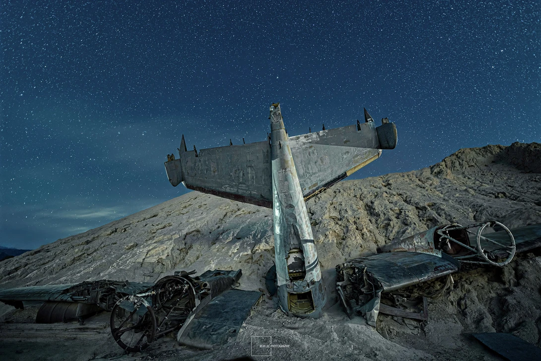 Abandoned aircraft wreckage tilted on a rocky hillside beneath a starry night sky.