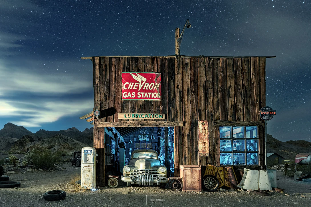 Abandoned wooden gas station structure with vintage Chevron signage and a classic car visible inside the garage bay.