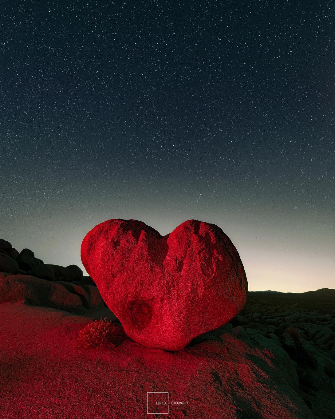 Large red heart-shaped rock formation silhouetted against a twilight sky with stars.