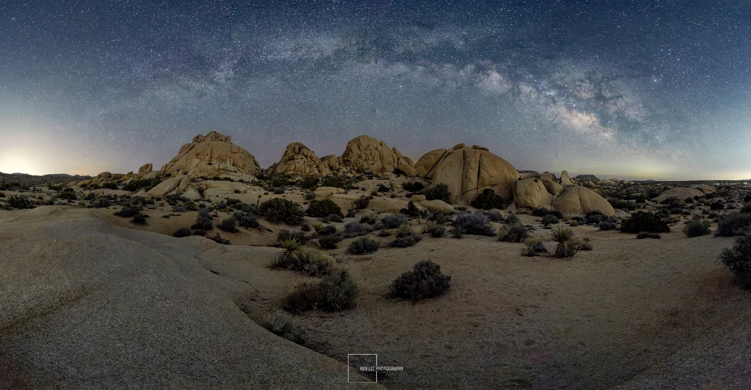 Desert landscape with large granite boulders under a starry night sky and visible Milky Way.