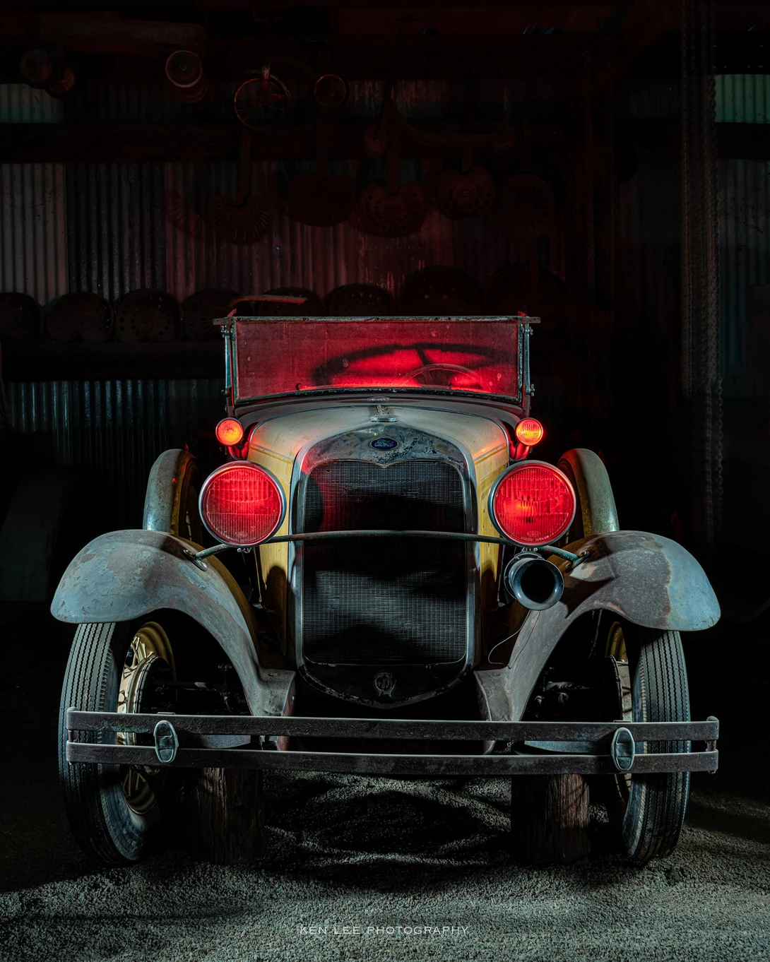 Front view of a vintage convertible automobile with red hood and headlights against a dark garage backdrop.