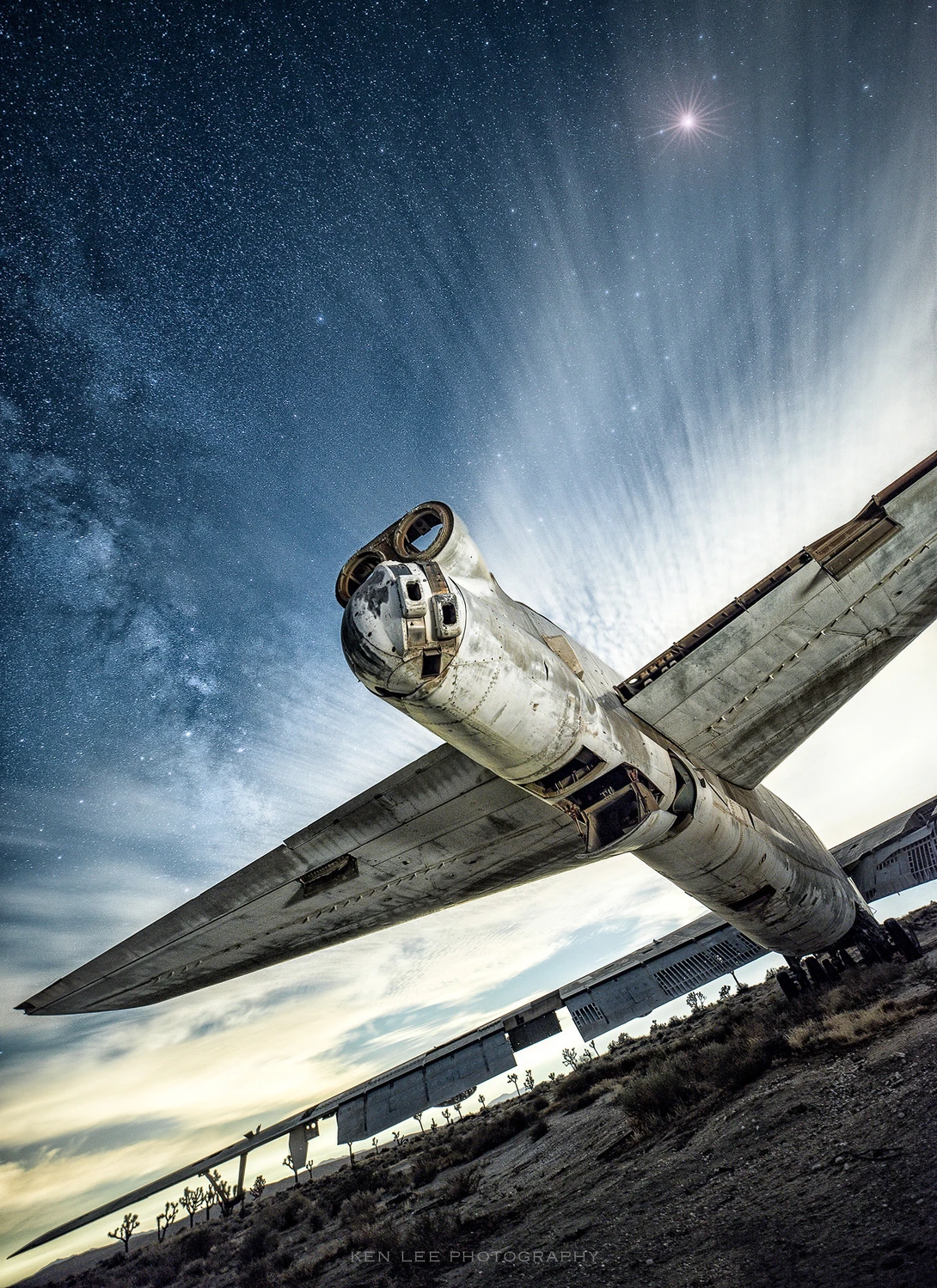 Abandoned aircraft photographed from below against a dramatic night sky with stars and light rays.