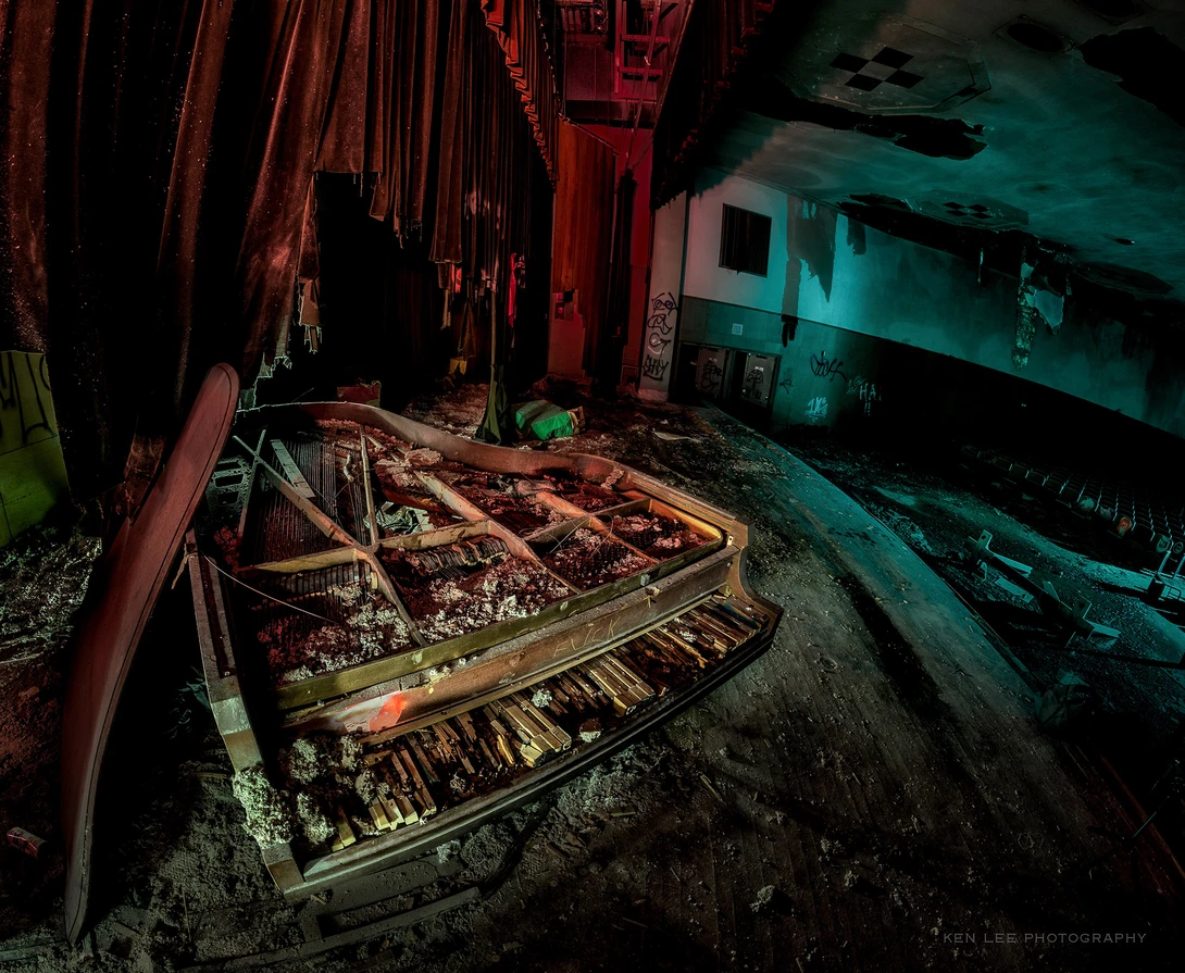 Abandoned interior with rusted metal boat hull and red industrial piping under moody colored lighting.