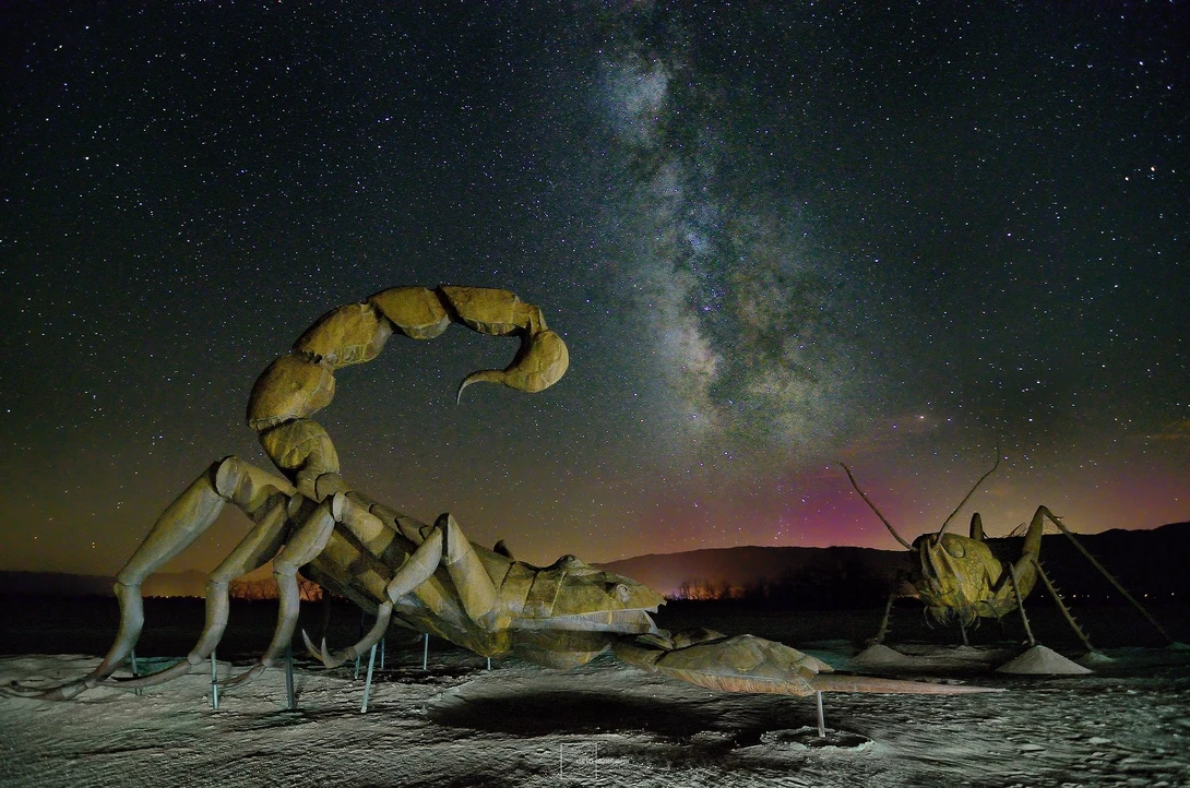 Giant illuminated scorpion sculpture beneath the Milky Way galaxy at night.