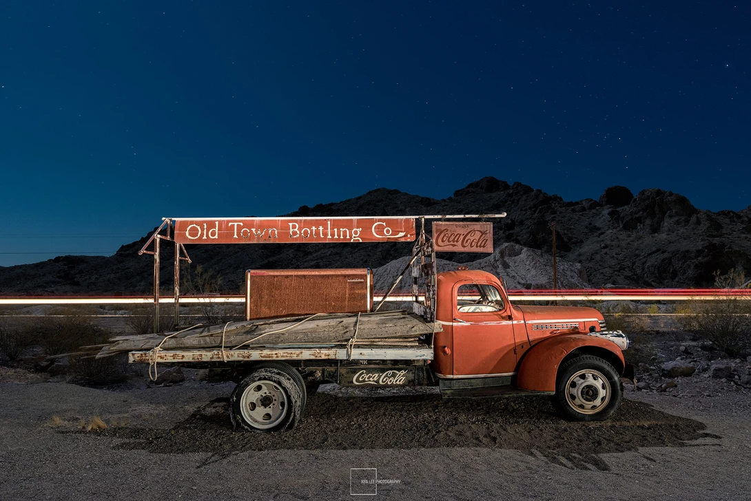 Vintage red truck and weathered bottling company building under clear night sky with stars.