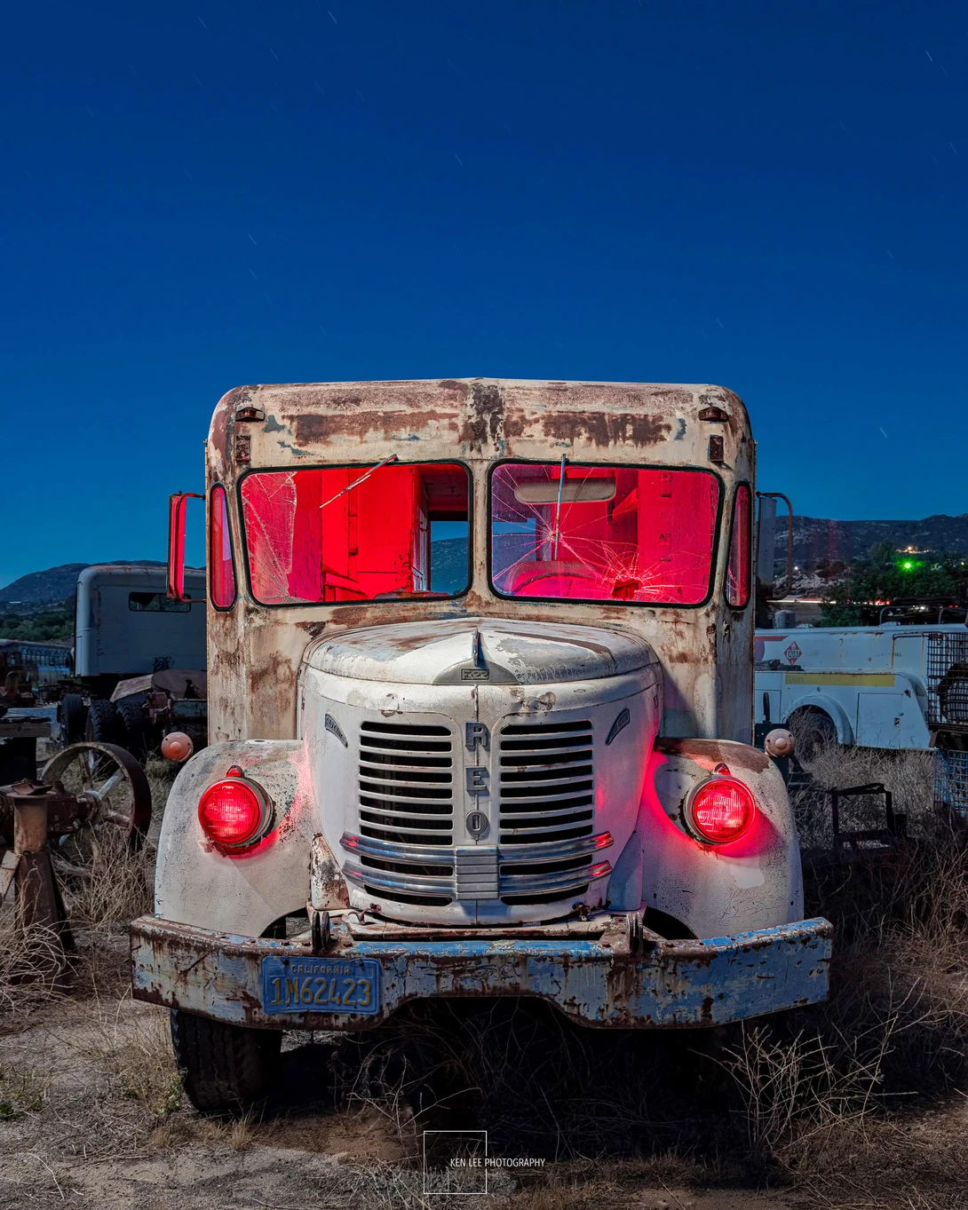 Weathered vintage truck photographed head-on against a clear blue sky, with red fabric covering windows and rusted metal details visible.