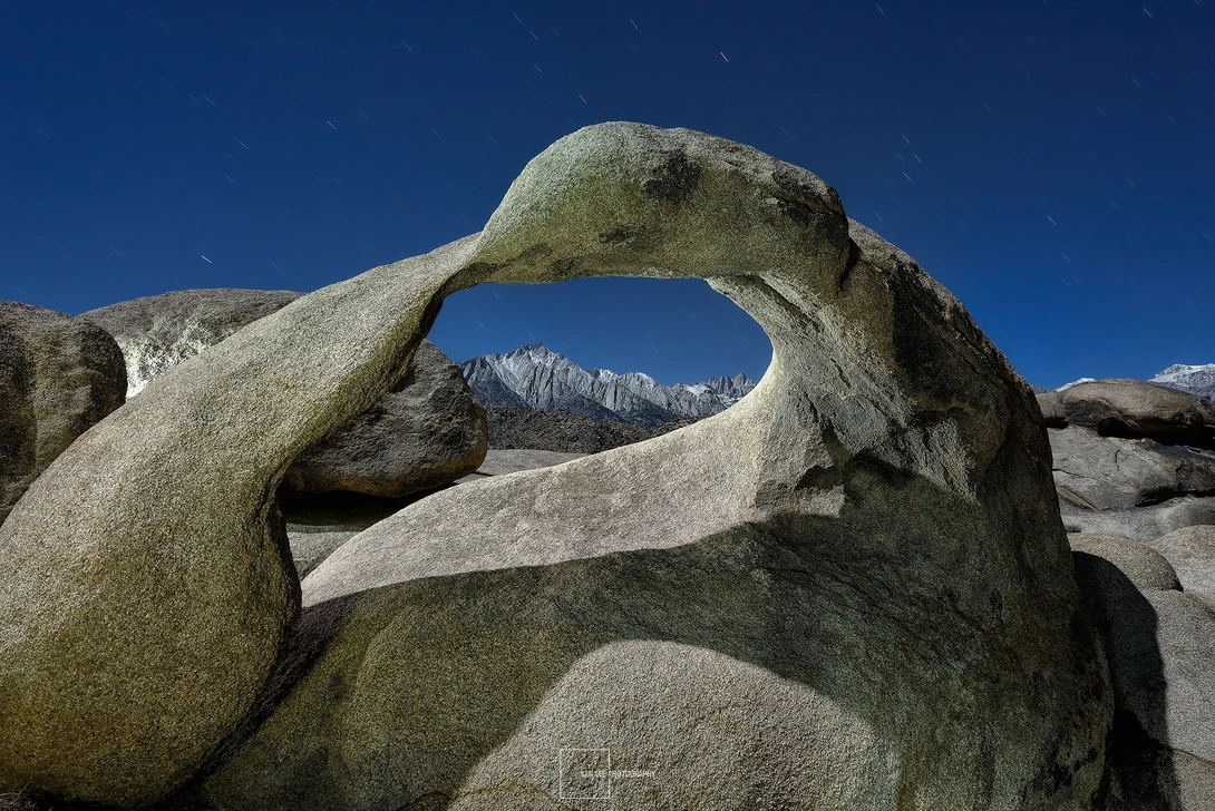 Large granite boulders frame a distant snow-capped mountain range through a natural rock opening.