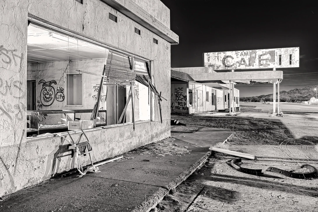 Abandoned roadside diner with broken windows and vintage signage in stark black and white photography.