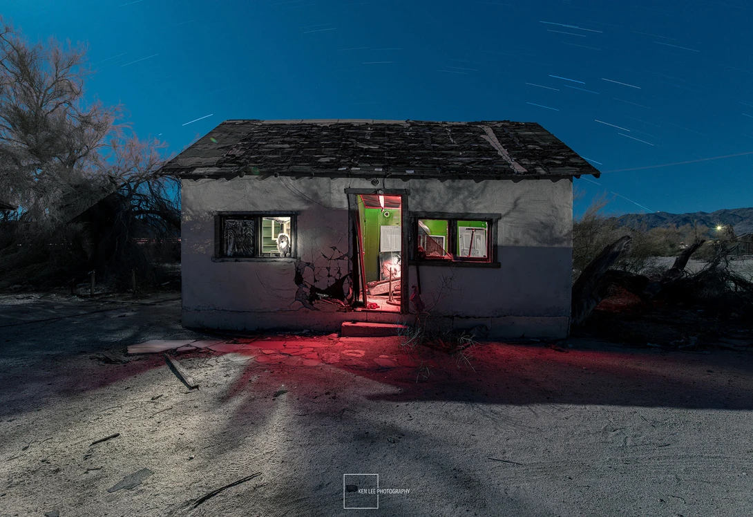 Abandoned small house illuminated by red light at dusk under clear blue sky.
