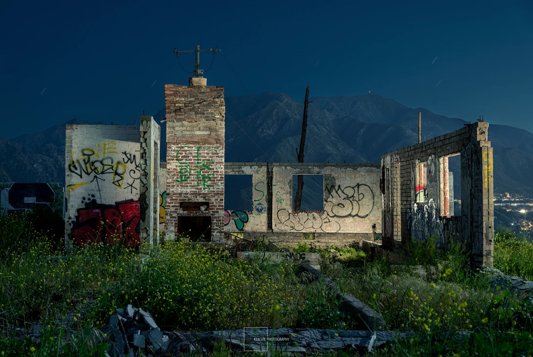 Abandoned brick building with graffiti against mountain backdrop at dusk.