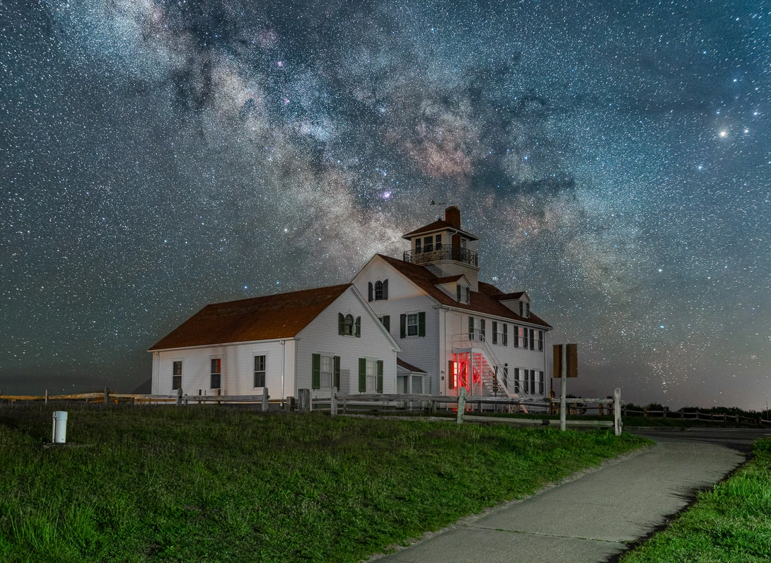 White farmhouse with red door beneath the Milky Way galaxy at night.