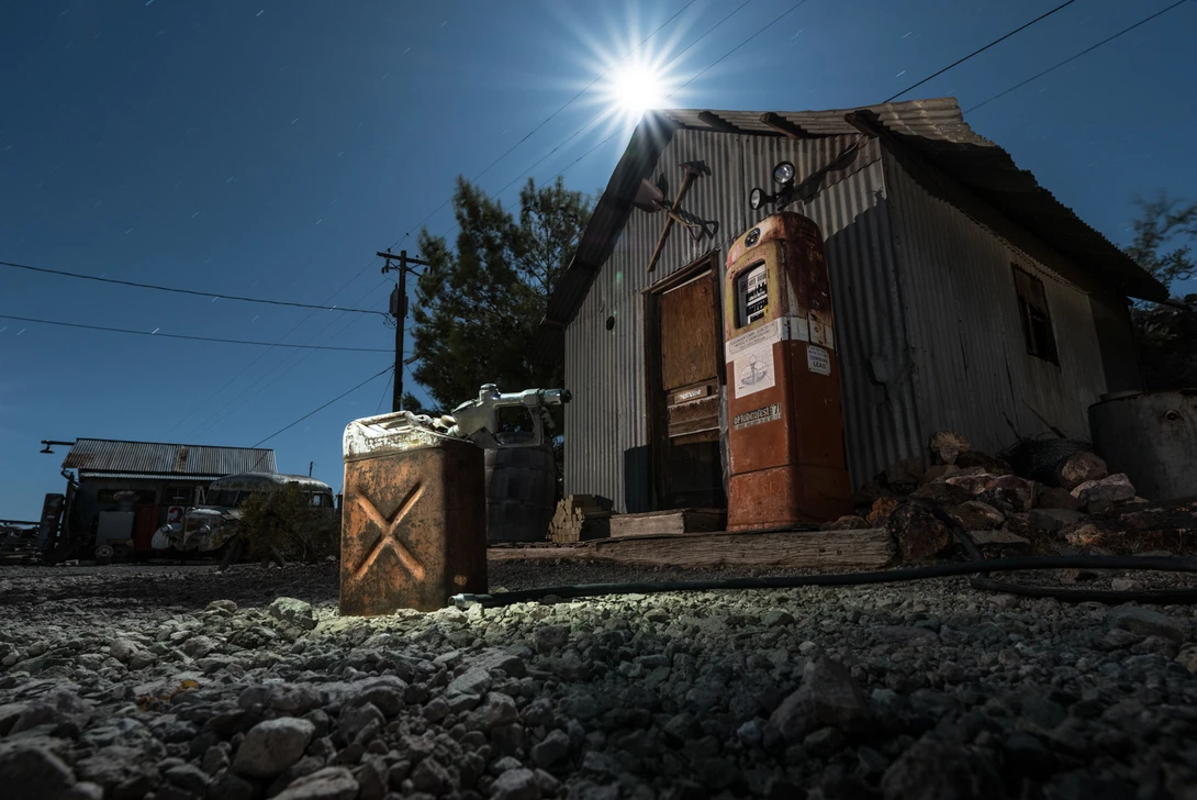 Dilapidated corrugated metal structure with rusted door under bright sunlight and clear blue sky.