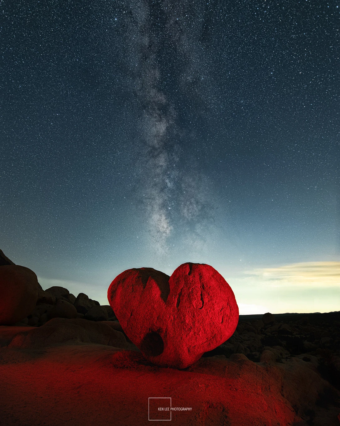 Large red heart-shaped structure illuminated against a night sky filled with stars and the Milky Way.