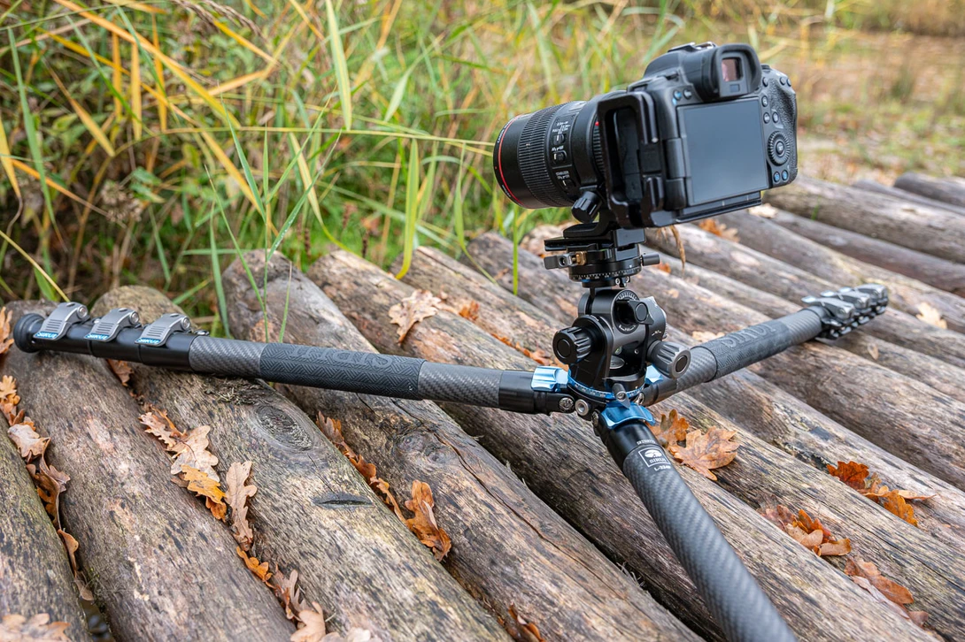 DSLR camera mounted on a tripod with an extended boom arm positioned over weathered logs.