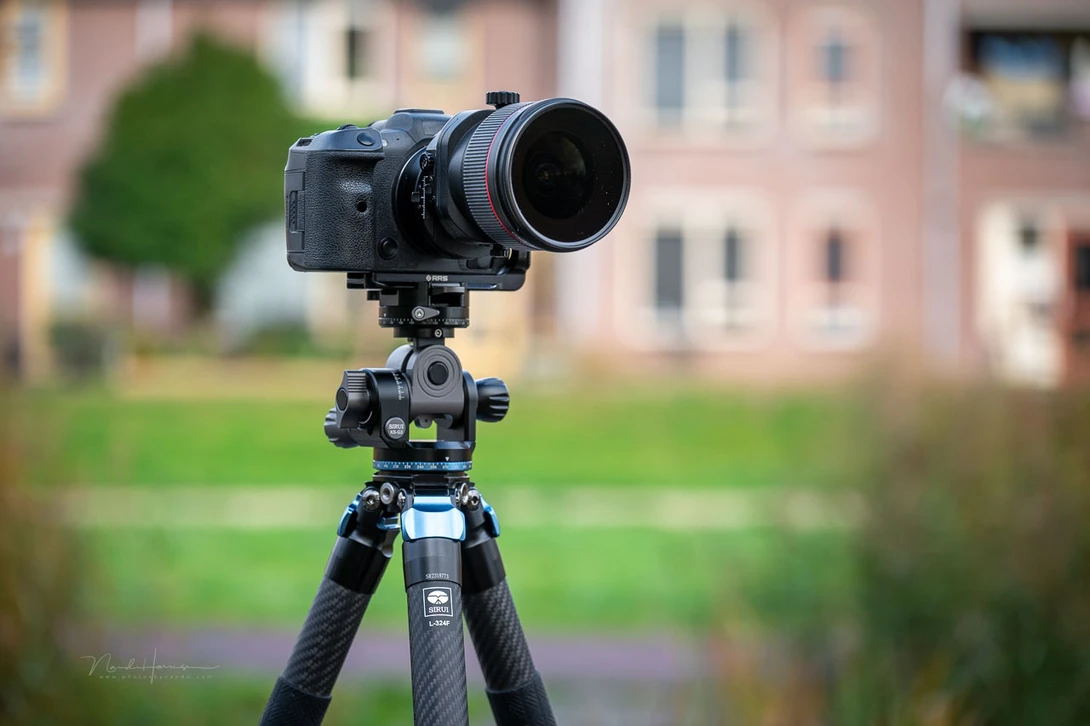 Professional DSLR camera mounted on carbon fiber tripod with telephoto lens, positioned in outdoor courtyard setting.