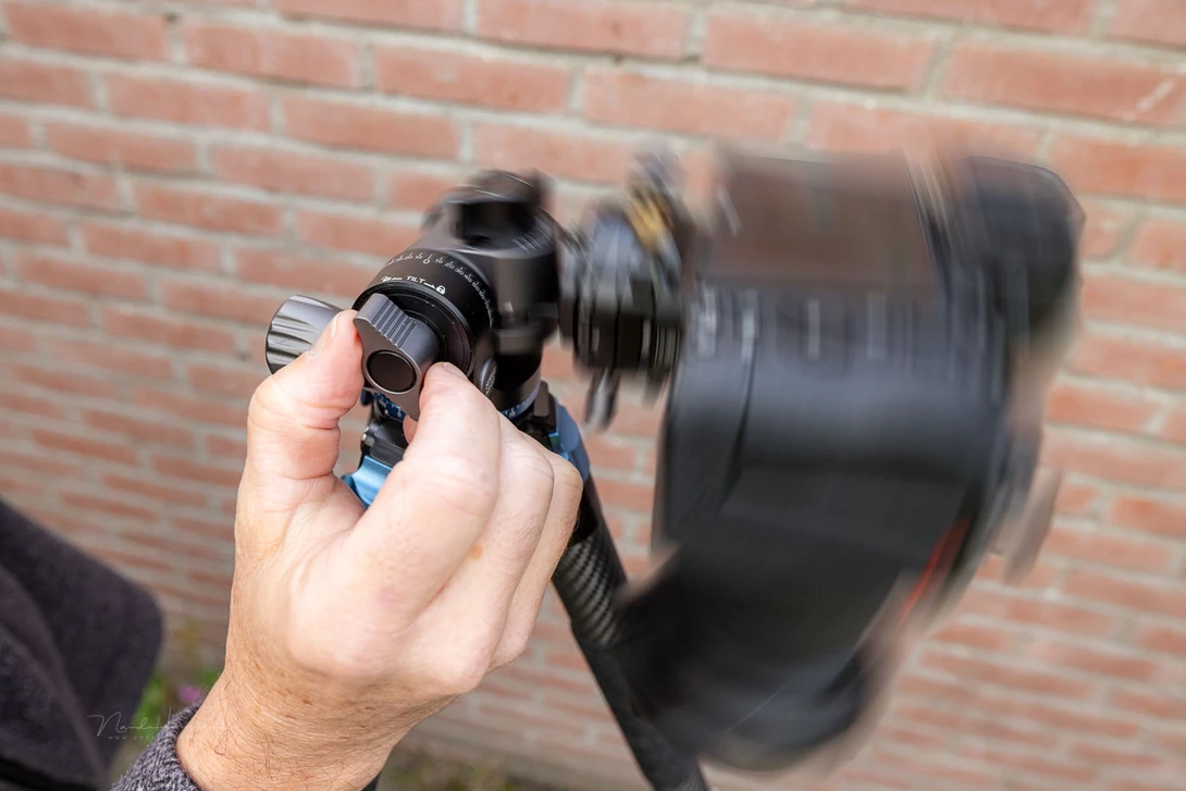 Photographer's hand holding a telephoto lens with motion blur against a brick wall background.