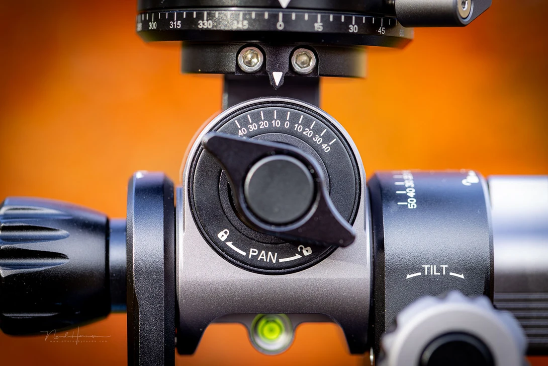 Professional tripod head with panoramic pan dial and tilt adjustment controls against an orange background.